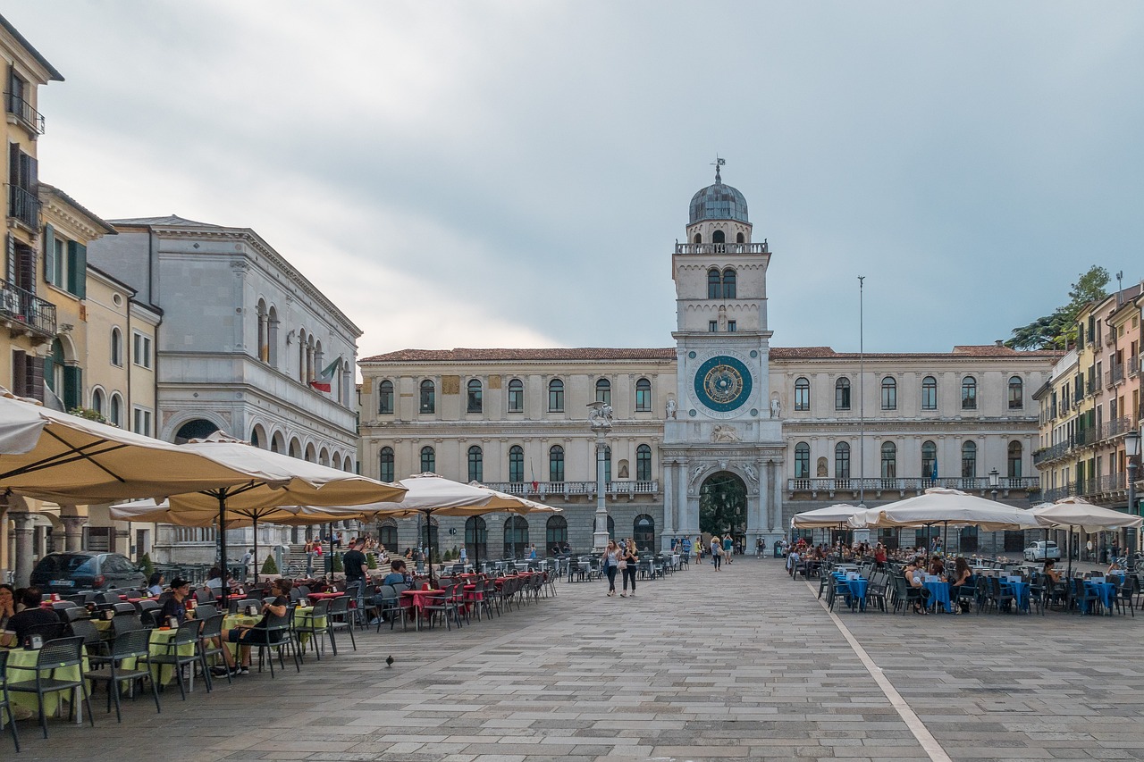 Piazza storica con architettura veneta e gente che passeggia nel sole.