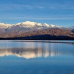 Vista panoramica del lago nascosto in Friuli, circondato da montagne e vegetazione lussureggiante.